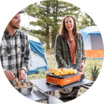 Two people smiling while cooking outdoors at campsite