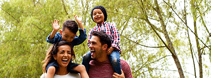 Cheerful parents laughing as two boys sit on mom and dad's shoulders.