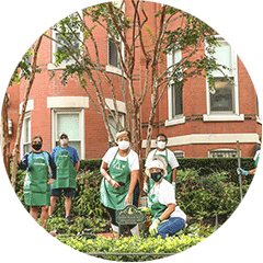 A group of people in face masks and green aprons tending to an urban garden.