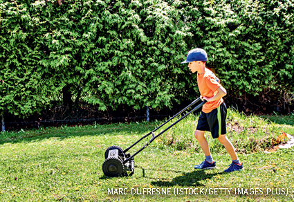 A young boy pushing a manual lawnmower